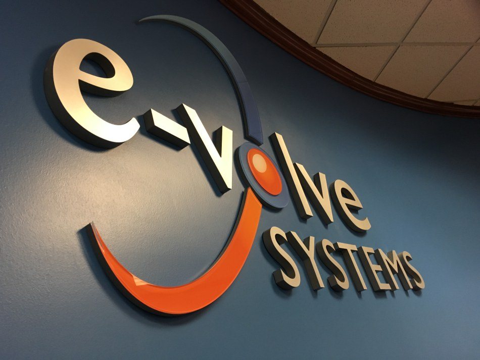 A dimensional e-volve Systems logo in brushed metal and orange, mounted on an office wall
